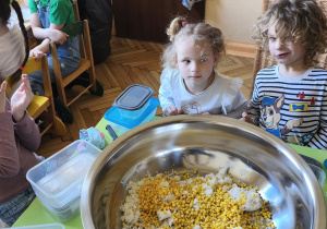 Zdjęcie przedstawia Oliwię, Mikołaja z grupy III oraz Klarę J. z grupy IV przy stoliku, na którym stoi misa ze składnikami sałatki.