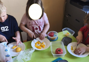 Na tym zdjęciu widać jedną z dziewczynek oraz Adasia W. i Mikołaja z grupy III, którzy kroją brzoskwinie na drobne kawałki.