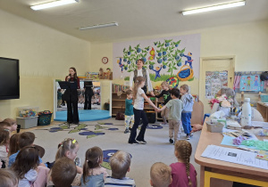 Zdjęcie przedstawia prowadzacego oraz wokalistkę wyśpiewującą różne imiona, zapraszając tym samym kolejne dzieci do zabawy w kole.