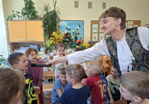 Na tym zdjęciu widać prowadzacego oraz dzieci prezentujące swoje umiejętności wokalne.