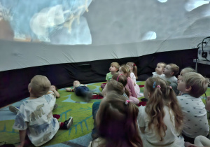 Zdjęcie przedstawia dzieci z grupy I oglądające film "Krecik w Kosmosie" wyświetlany w kopule.