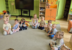 Zdjęcie przedstawia dzieci siedzące na dywanie słuchające bajki.