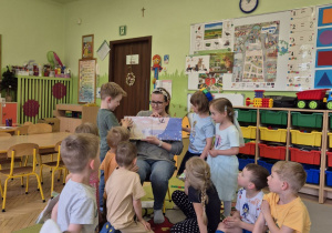 Na tym zdjęciu widać mamę Adasia, która pokazuje dzieciom ilustracje w książeczce.