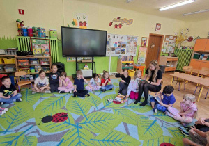 Na tym zdjęciu widać dzieci siedzące w kole oraz mamę Filipa, która czyta dzieciom książkę.
