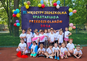 Na tym zdjęciu widać dzieci stojące przy banerze informującym o spartakiadzie.