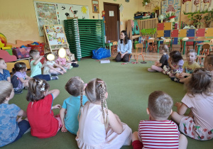 Zdjęcie przedstawia dzieci siedzące na dywanie w kole oraz mamę Mikołaja.