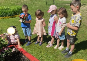 Na tym zdjęciu widać kilkoro dzieci: z grupy I, II i III przed rabatą, na której będą sadzić kwiaty.