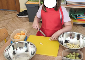 Zdjęcie przedstawia jedną z dziewczynek z grupy III krojącą owoce w drobną kostkę.
