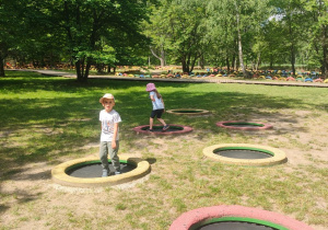 Zdjęcie przedstawia dwoje dzieci bawiących się na trampolinach.