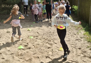 Zdjęcie przedstawia dzieci biorące udział w konkurencji sportowej: przenoszenie piłeczek na krążkach.