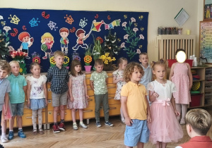 Zdjęcie przedstawia Oliwię i Mikołaja recytujących wierszyk oraz pozostałe dzieci stojące w półkolu.