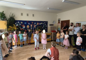 Zdjęcie przedstawia Wojtka i Martę recytujących wierszyk oraz pozostałe dzieci stojące w półkolu, a także rodziców przybyłych na uroczystość.