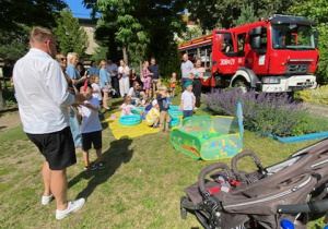 Zdjęcie przedstawia dzieci oraz rodziców w strefie zabawa z wodą oraz w tle wóz strażacki.
