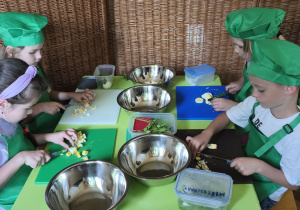 Zdjęcie przedstawia Marcelinkę Ł., Julka, Wandę i Stasia W. z grupy IV, którzy siekają jajka.