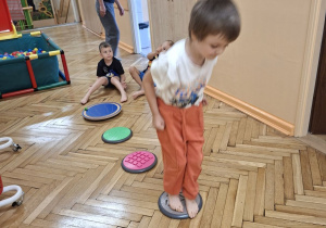 Na tym zdjęciu widać Adasia z grupy II, która wykonuje ćwiczenia stóp z wykorzystaniem krążków masujących.