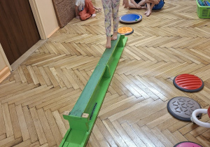 Zdjęcie przedstawia Jagodę L. z grupy III podczas ćwiczeń równoważnych z wykorzystaniem ławeczki gimnastycznej.