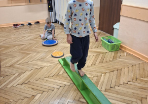 Zdjęcie przedstawia Marcela z grupy III podczas ćwiczeń równoważnych z wykorzystaniem ławeczki gimnastycznej.