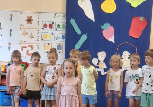 Na tym zdjęciu widać Lenę T. z grupy I recytującą wierszyk oraz inne dzieci występujące w przedstawieniu stojące z tyłu.