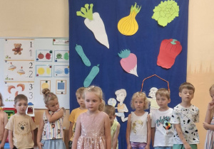 Na tym zdjęciu widać Natalkę M. z grupy II recytującą wierszyk oraz inne dzieci występujące w przedstawieniu stojące z tyłu.