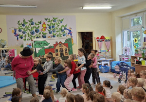 Zdjęcie przedstawia kilkoro dzieci z grupy IV wraz z aktorką podczas prezentacji wiersza "Rzepka".