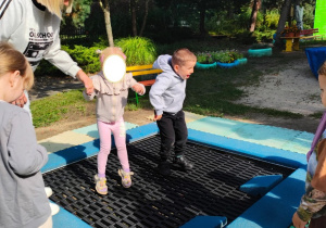 Zdjęcie przedstawia troje dzieci z grupy I podczas zabawy na trampolinie.
