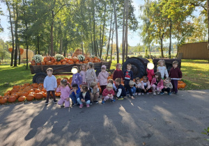 Zdjęcie przedstawia dzieci przy traktorze z wozem wypełnionym dyniami.