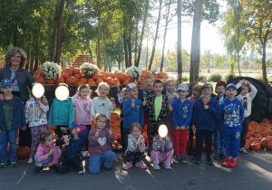 Zdjęcie przedstawia dzieci przy traktorze z wozem wypełnionym dyniami.