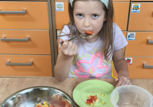 Zdjęcie przedstawia jedną z dziewczynek degustującą przygotowaną przez siebie sałatkę.