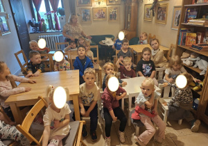 Zdjęcie przedstawia dzieci z grupy I i II siedzące przy stolikach w oczekiwaniu na przedstawienie.