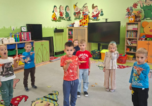 Zdjęcie przedstawia kilkoro dzieci z grupy III biorących udział w zabawie ruchowej połączonej z ćwiczeniami oddechowymi.