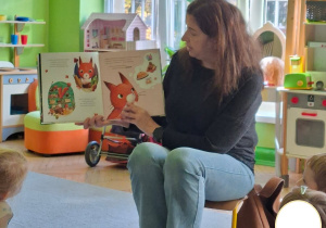 Na tym zdjęciu widać panią bibliotekark, która czyta dzieciom książeczkę.