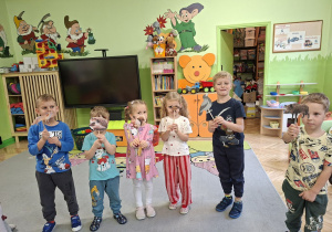 Zdjęcie przedstawia kilkoro dzieci tworzących scenkę z wykorzystaniem kukiełek zwierząt występujących w bajce.